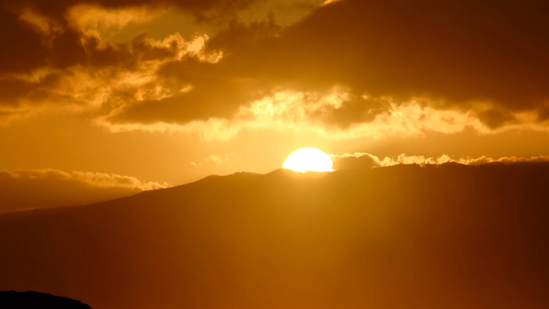 El sol poniéndose tras la silueta de la cordillera Waiʻanae en el lado oeste de Oʻahu, con un remero visible en el agua